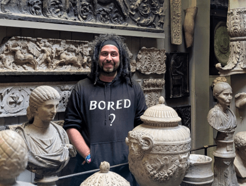 Simon Farid stands in the Dome area of Sir John Soane's Museum. He is working a black hoody which reads 'Bored?' and is surrounded by sculptures.