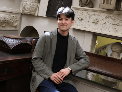 Kanto Ohara Maeda sits on a chair in Sir John Soane's Drawing office, he is smiling at the camera